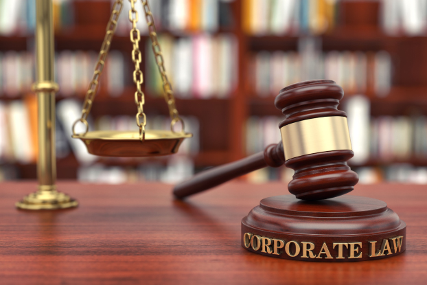 A close-up of a gavel resting on a sound block that says "corporate law." There is a scale in the background.