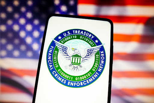In this photo illustration, the United States Financial Crimes Enforcement Network (FinCEN) logo is displayed on a smartphone screen with a United States flag in the background