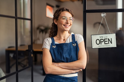 A woman standing outside of a shop with an "open" sign on the window.